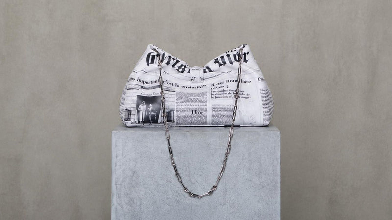Dior newspaper print slouchy chain-strap bag from Jonathan Anderson's Cruise 2027 collection, as seen at Phoenix Style.