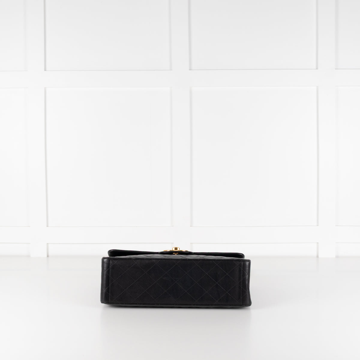Bottom of Black preloved Chanel Vintage 34 Maxi Lambskin Single Flap bag on white background.