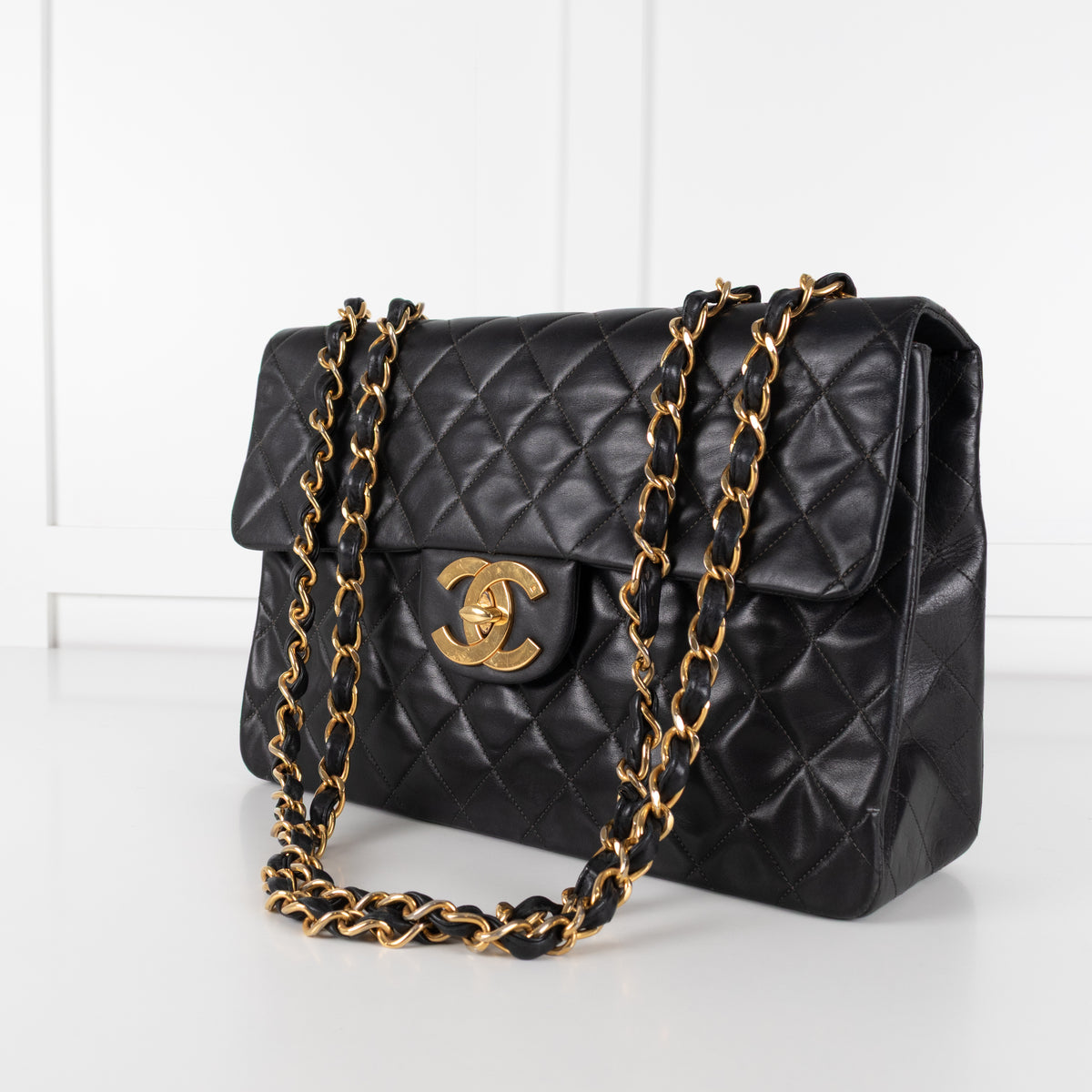 Close up of Black Chanel Vintage 34 Maxi Lambskin Single Flap bag on white background with gold hardware.