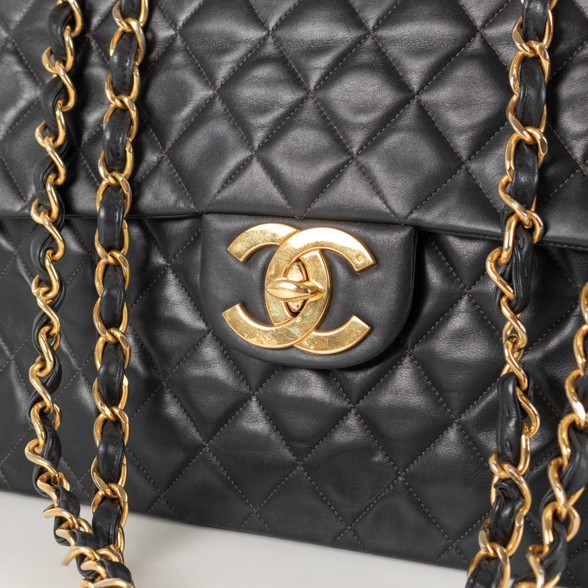 Close up of Black Chanel Vintage 34 Maxi Lambskin Single Flap bag on white background with gold hardware and CC clasp.