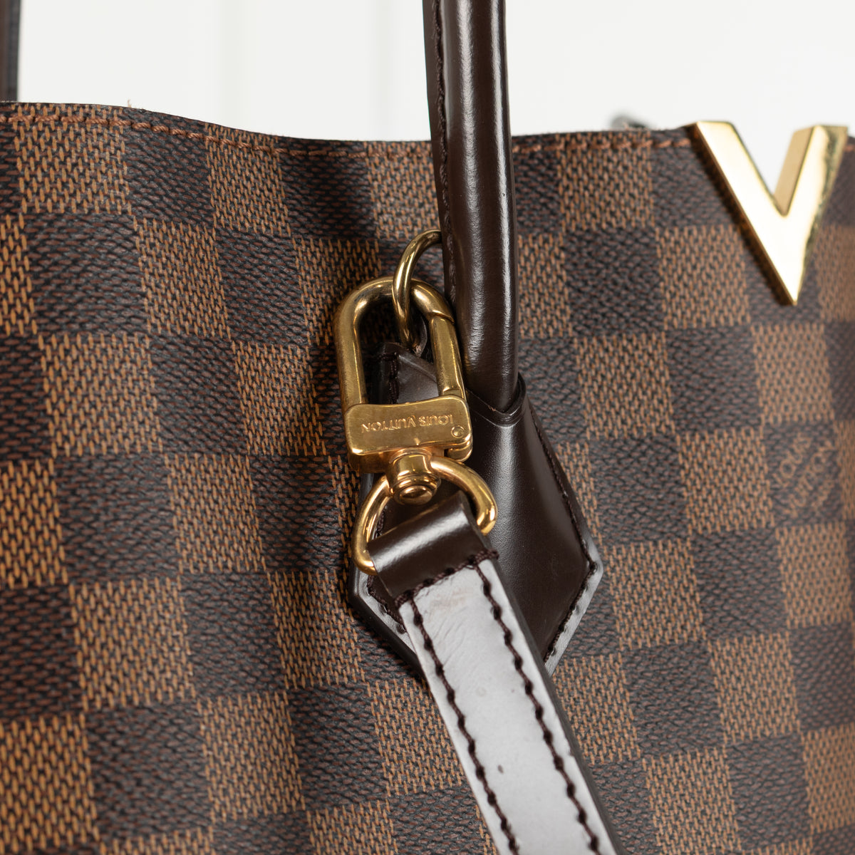 Clasps of gold hardware clips on Louis Vuitton Damier Kensington Tote bag. 