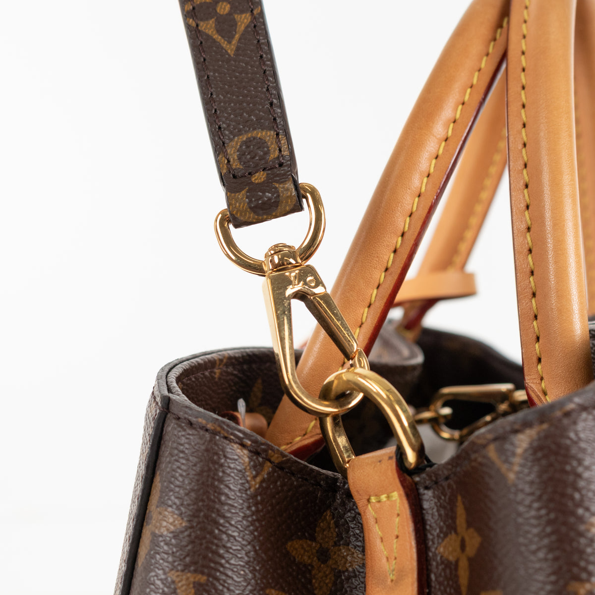 Close up of brown leather and gold hardware detail on Louis Vuitton Monogram Canvas Montaigne MM bag.