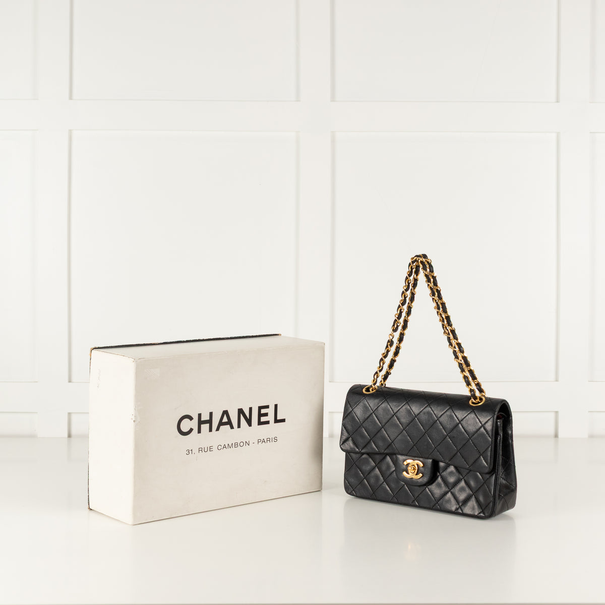 Black quilted vintage Chanel handbag with gold chain and Chanel box on a white background