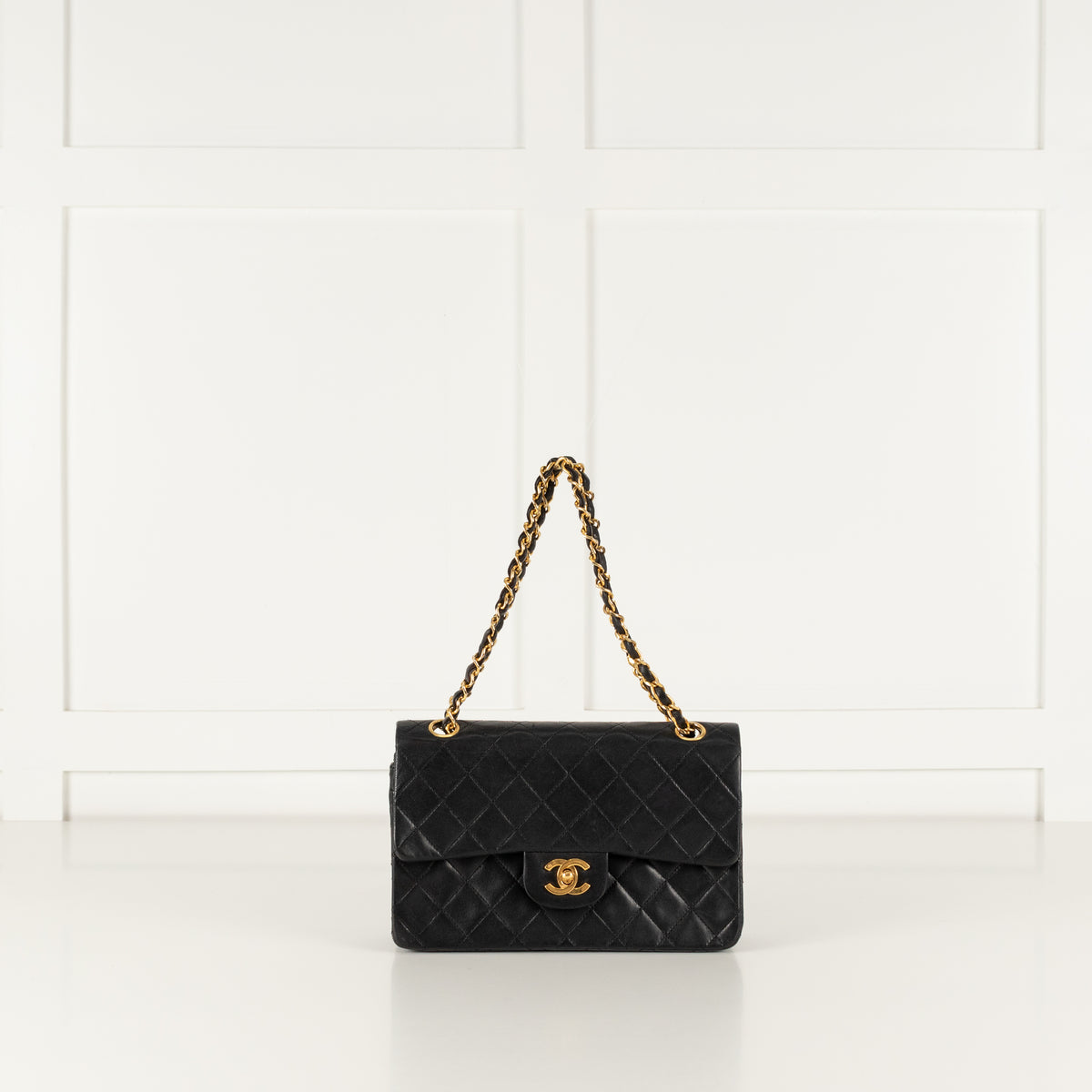 Vintage Chanel black quilted handbag with gold chain strap on a white background.