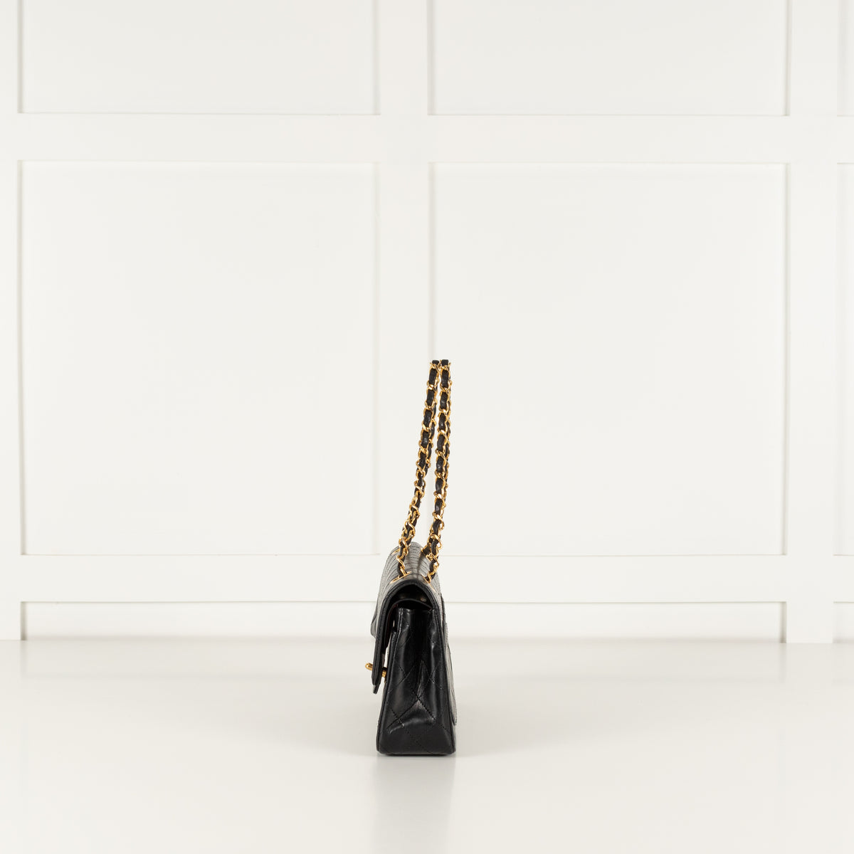 Side profile of a Black vintage Chanel handbag with gold chain strap on a white background