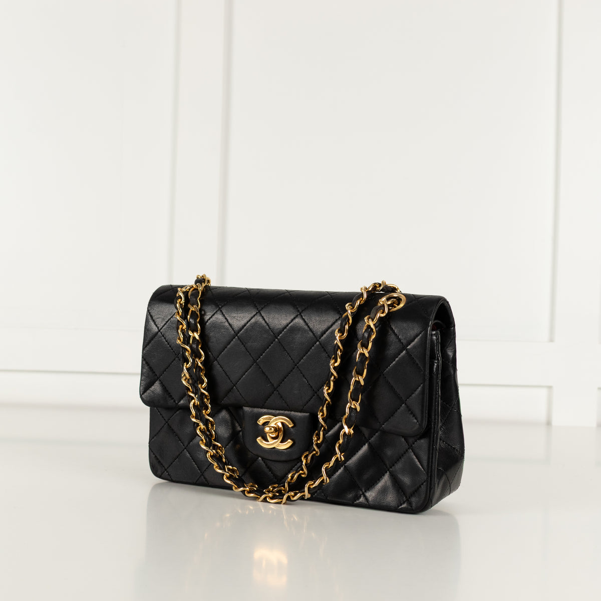Black quilted vintage Chanel handbag with gold chain and clasp on a white background