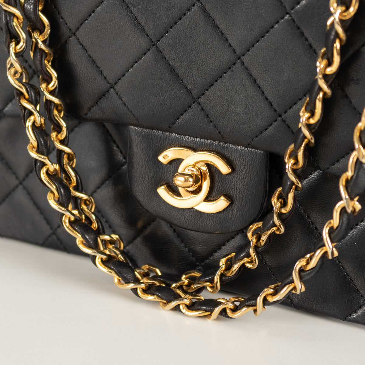Black vintage Chanel quilted handbag with gold chain strap and logo on a white background in Phoenix style shop.