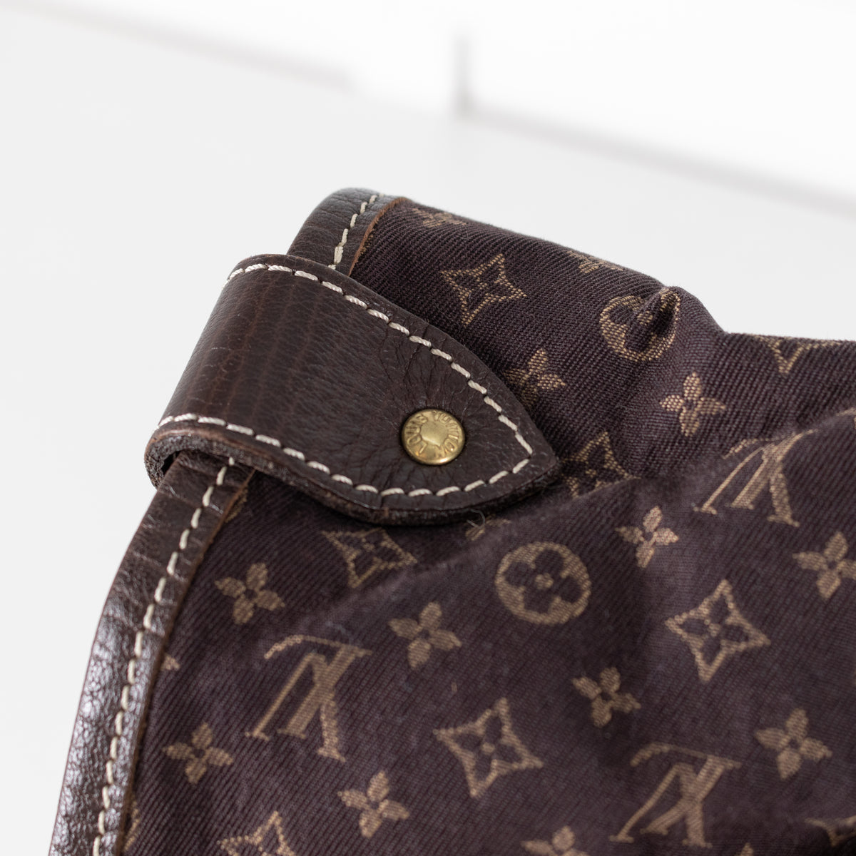 Close-up of a brown Louis Vuitton handbag fabric with a patterned design and a gold button on a white background.