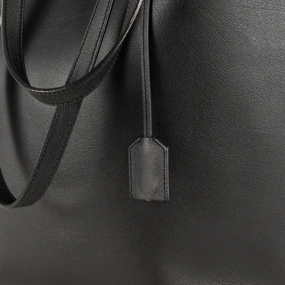 Close-up of a black saint laurent leather bag with a strap and tag.