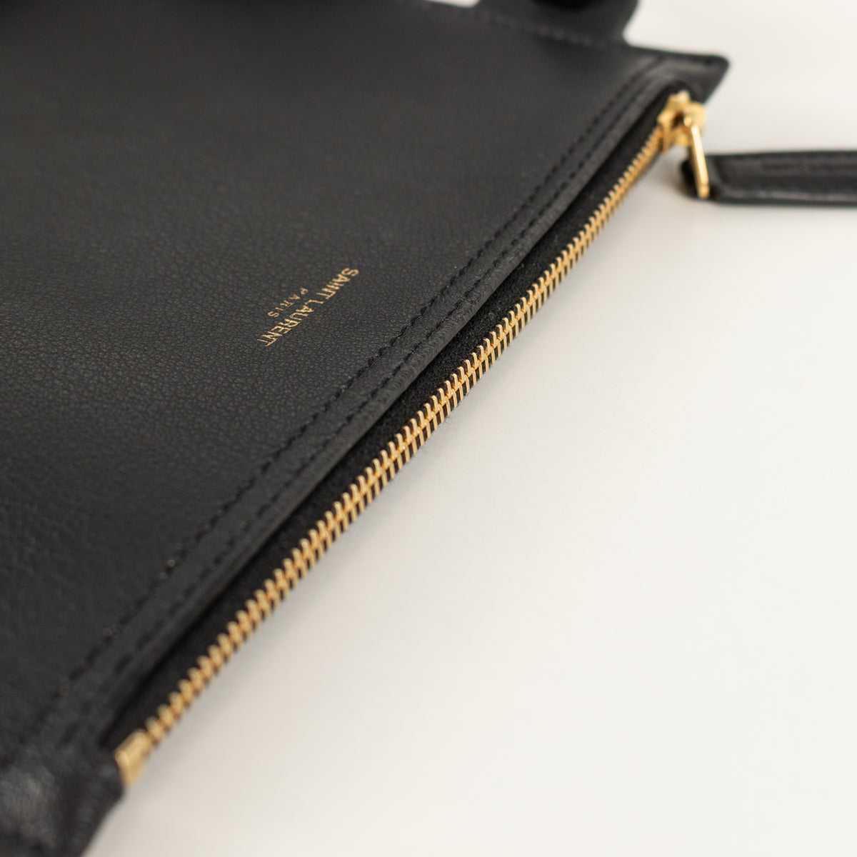 Black leather saint laurent pouch with gold zipper on a white background. 