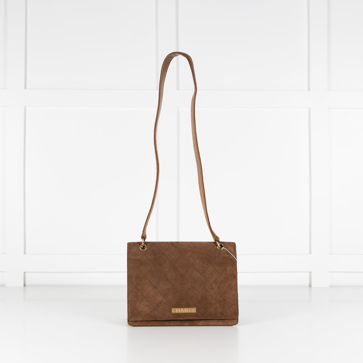 Brown leather Chanel flap handbag with a strap on a white background.
