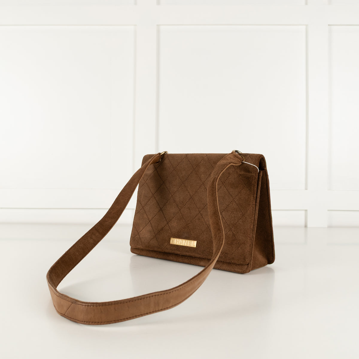 Brown quilted Chanel handbag with a gold clasp on a white surface.