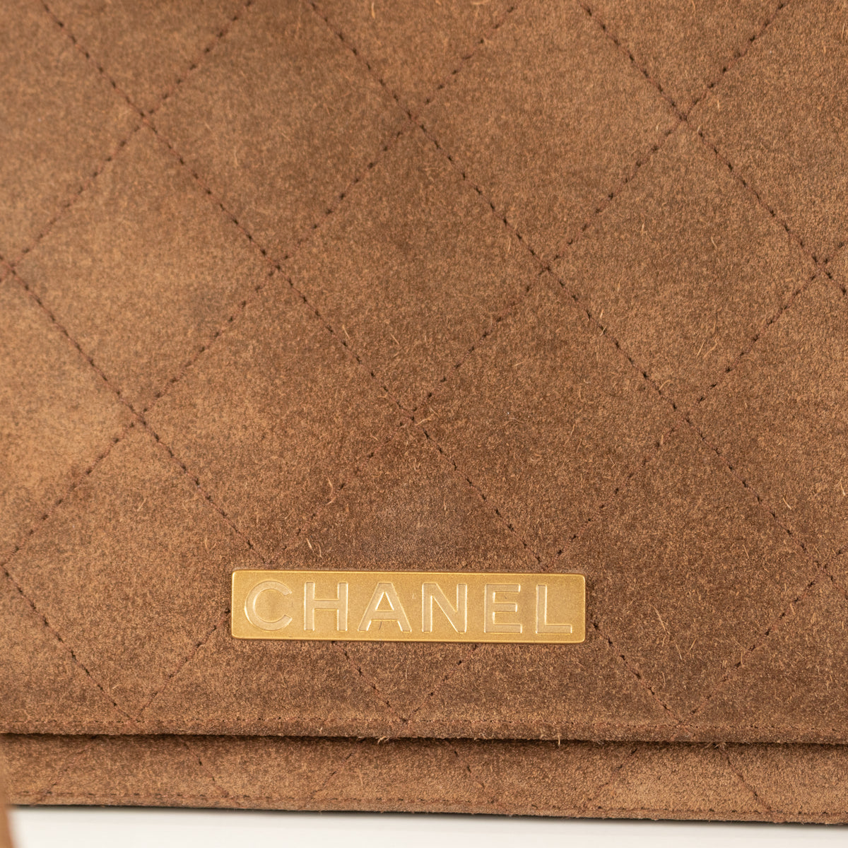 Close-up of a preloved brown quilted handbag with a gold Chanel logo tag.