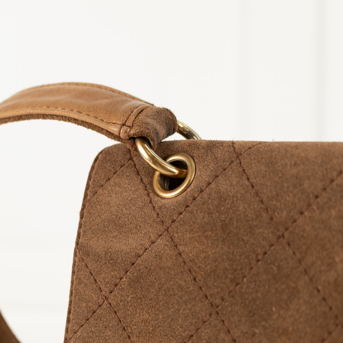 Close-up of a Chanel brown quilted handbag with a gold metal ring on a white background