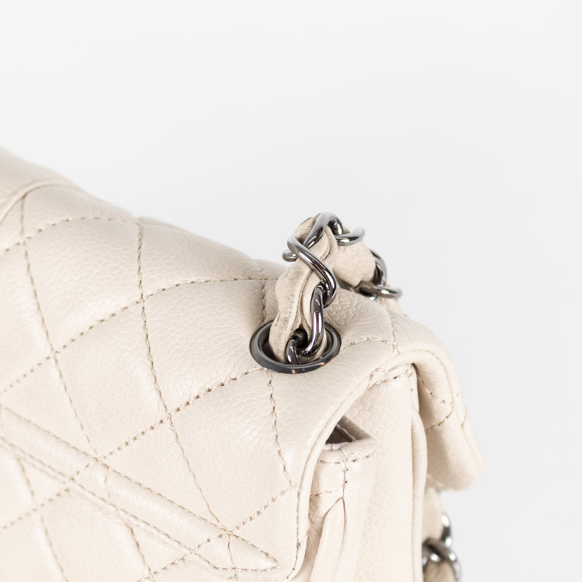 Close-up of a beige quilted handbag with a silver chain detail on a white background