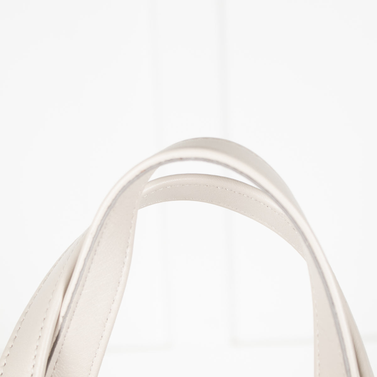 Close-up of a white handbag handle on a light background.