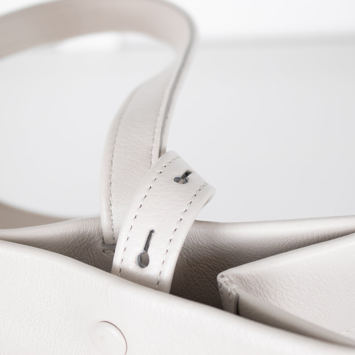 Close-up of a white leather bag strap with stitching details on a white background
