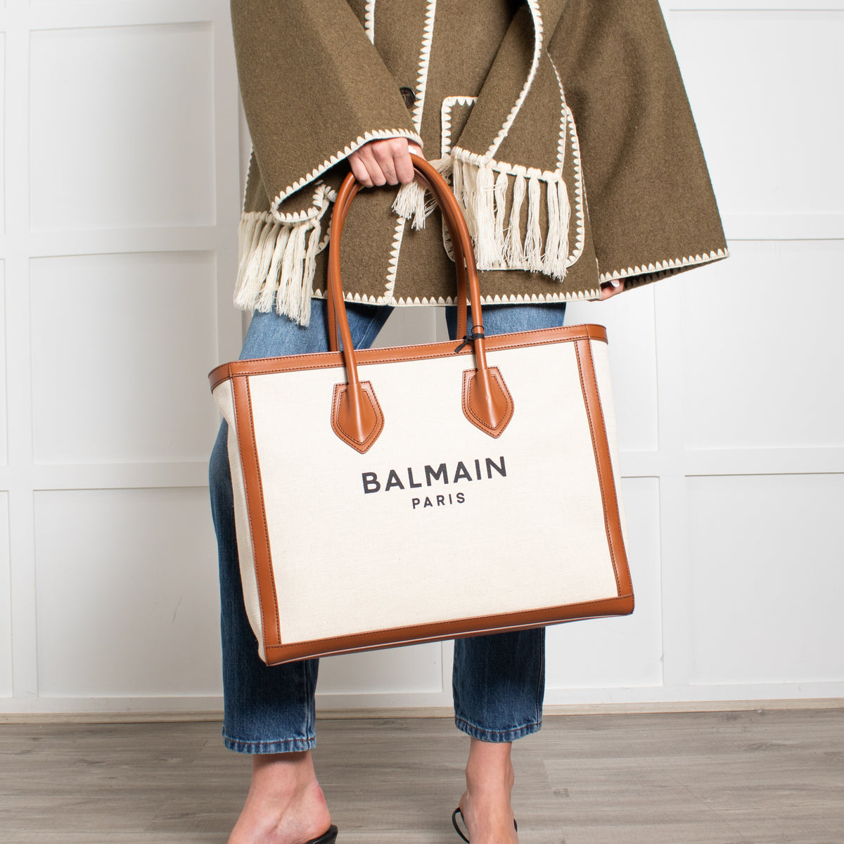 Person holding a Balmain Paris tote bag with a wooden floor and white wall background