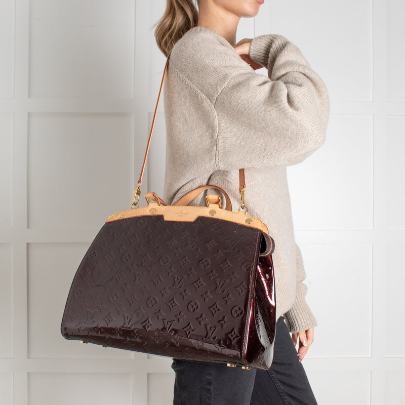 person holdinga mongram Louis Vuitton brown leather handbag against a white wall.