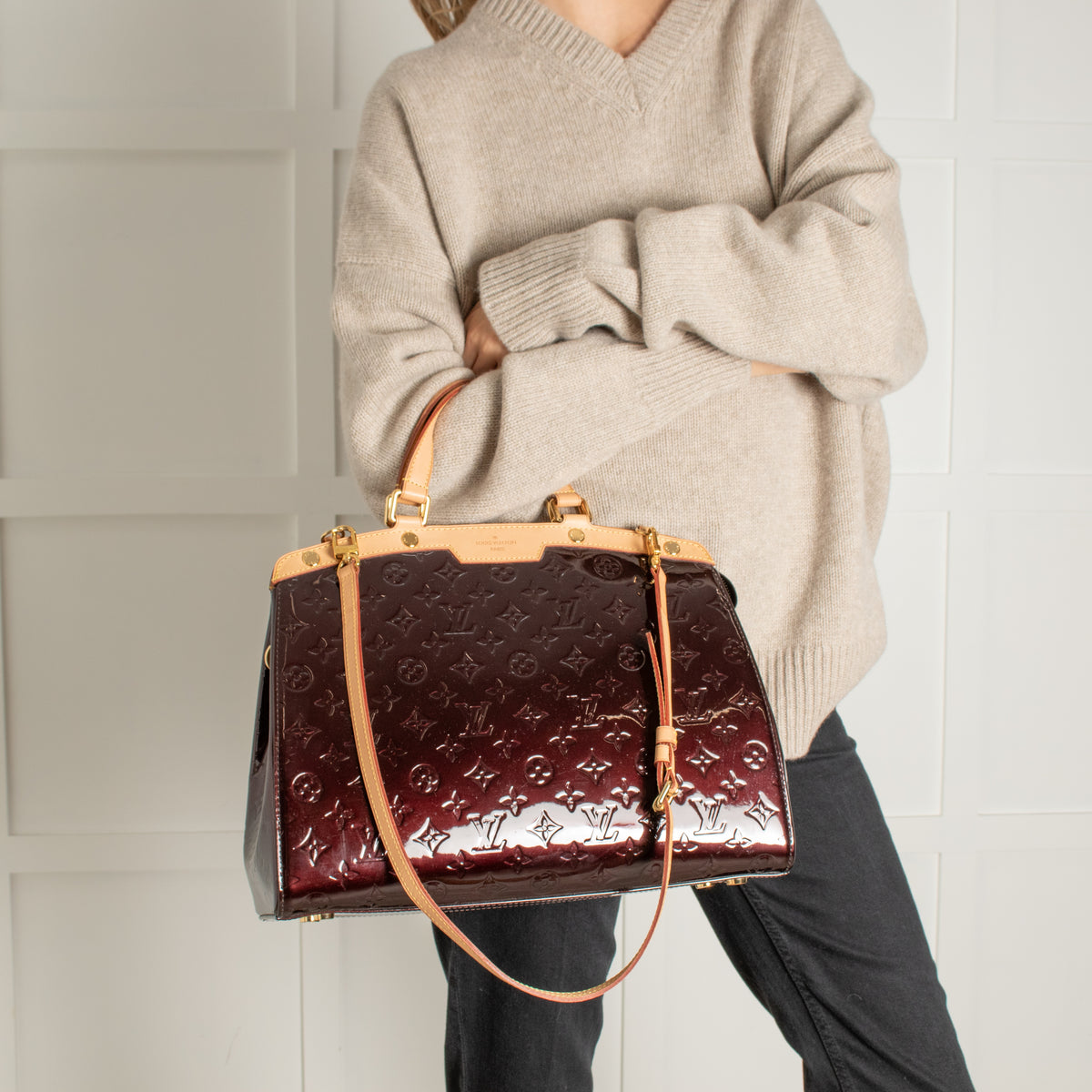 Person holding a monogram burgundy Louis Vuitton brown leather handbag. 