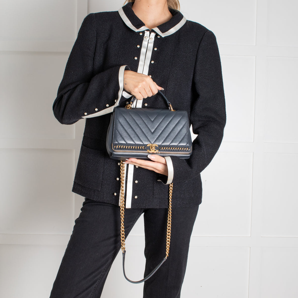 Model holding Navy Preloved Chanel Handbag with gold chain on white background.