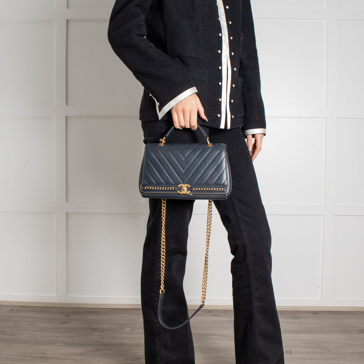 Person holding from top handle Navy Preloved Chanel Handbag on white background.