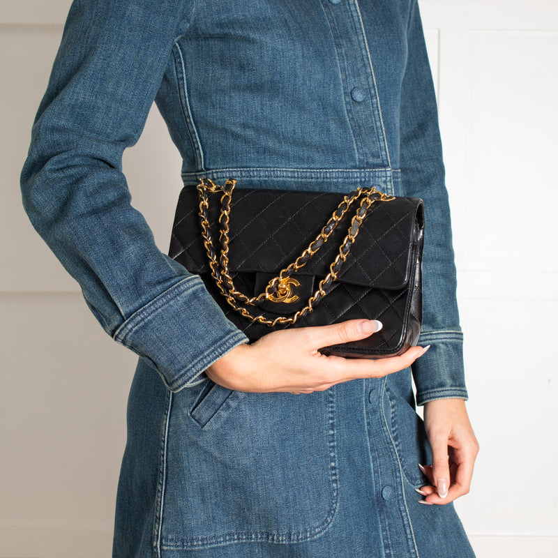 Person holding a black Vintage Chanel handbag with gold chain detail, wearing a denim jacket.