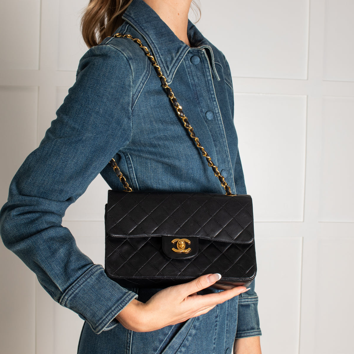 Person holding a black quilted vintage Chanel handbag with a gold chain strap against a white background